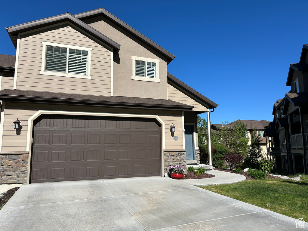 View of front of house featuring an attached garage, driveway, a shingled roof, and stone siding
