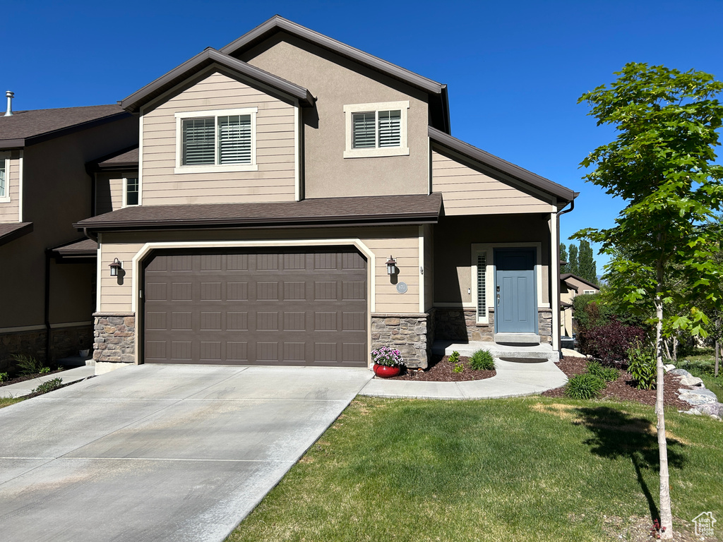 View of front facade featuring a garage, a front lawn, driveway, and stone siding
