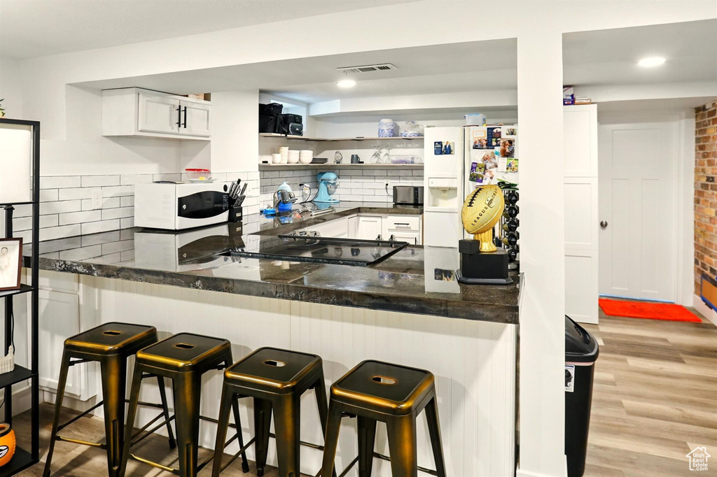 Kitchen featuring backsplash, visible vents, white cabinets, a peninsula, and white appliances