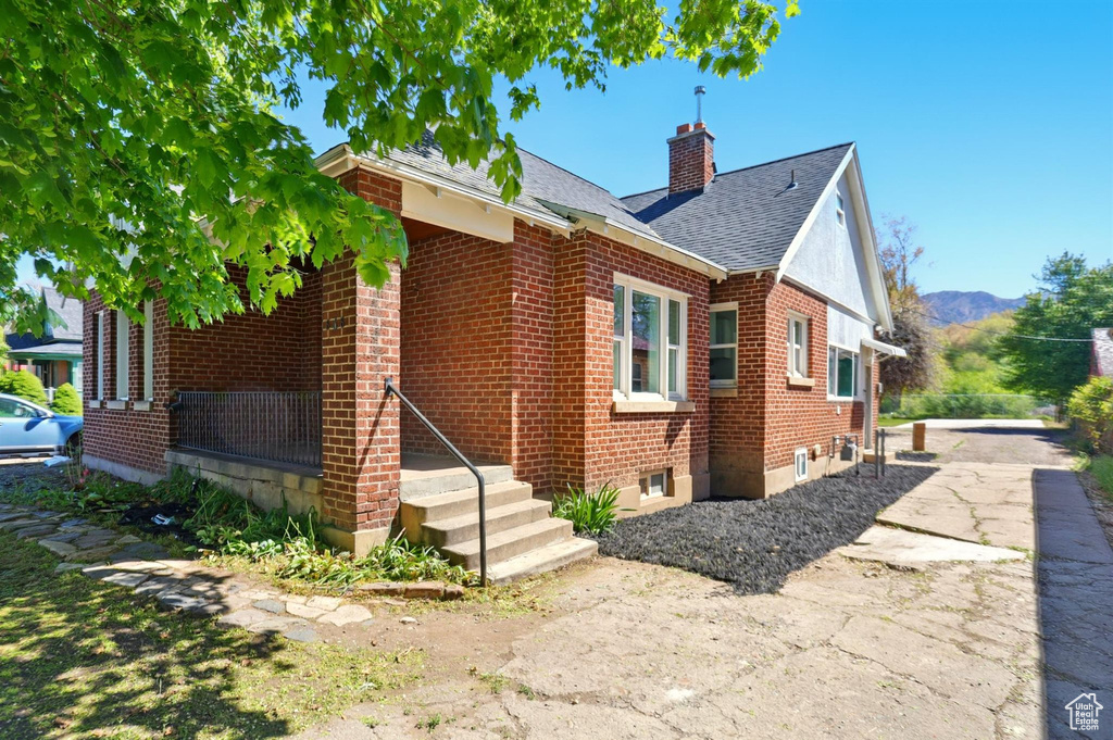 Exterior space featuring roof with shingles, a mountain view, a chimney, and brick siding