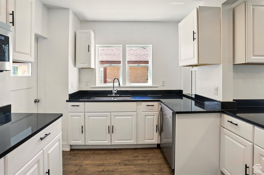 Kitchen with a sink, dark wood-style flooring, white cabinets, and dark countertops