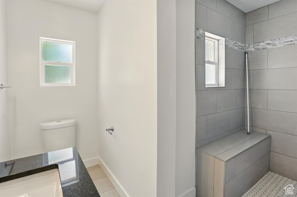 Full bath featuring toilet, baseboards, tiled shower, and a wealth of natural light