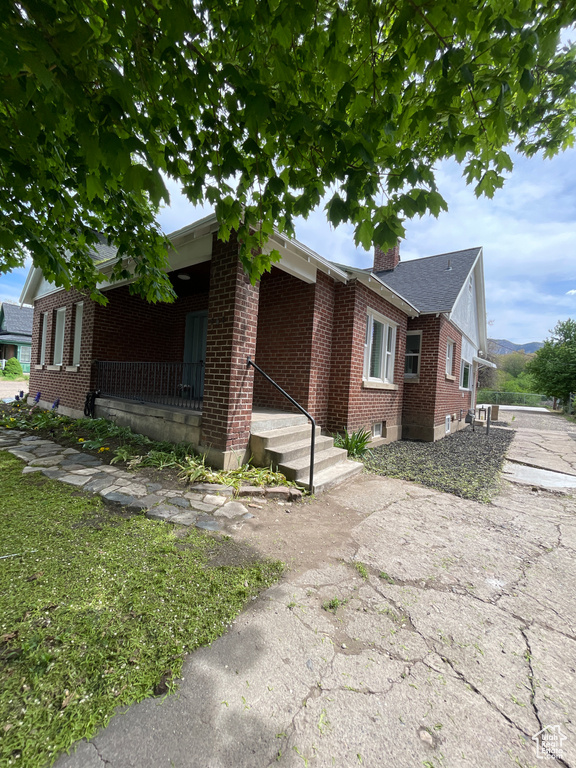 View of front of home with covered porch, a chimney, and brick siding