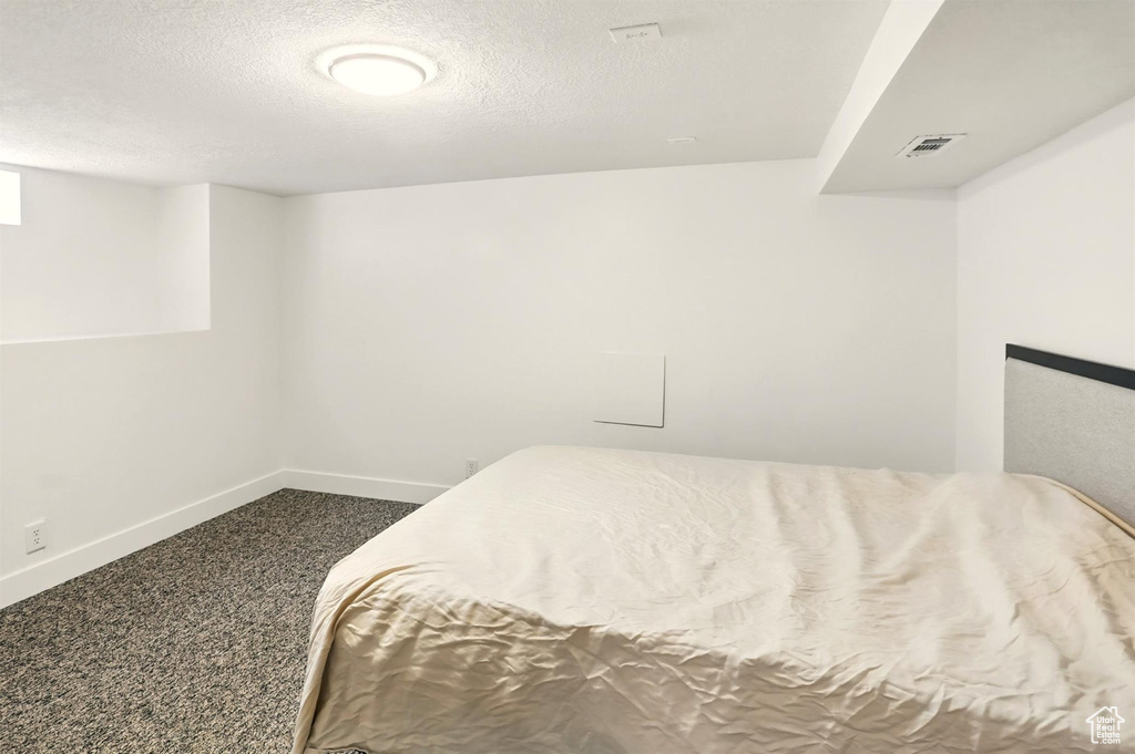 Bedroom with a textured ceiling, baseboards, visible vents, and dark carpet
