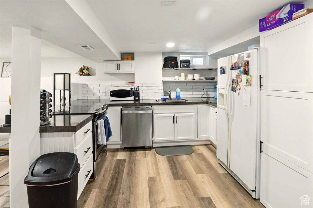 Kitchen with open shelves, appliances with stainless steel finishes, dark countertops, and light wood-style flooring