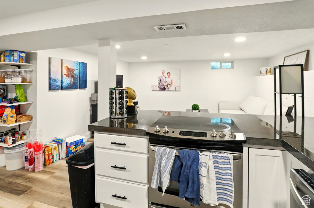 Kitchen featuring dark countertops, light wood finished floors, white cabinetry, and stainless steel range with electric cooktop