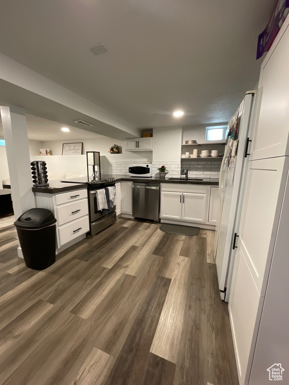 Kitchen with a sink, dark wood-style flooring, white cabinetry, dark countertops, and appliances with stainless steel finishes