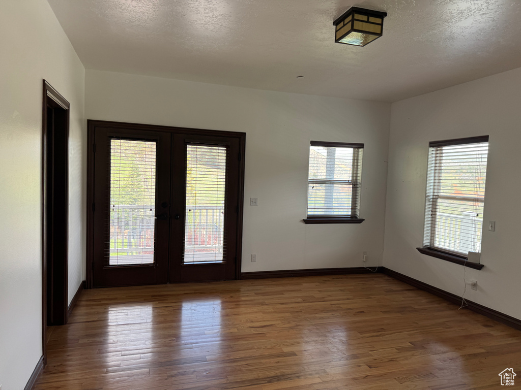 Empty room featuring french doors, healthy amount of natural light, wood finished floors, baseboards, and a textured ceiling