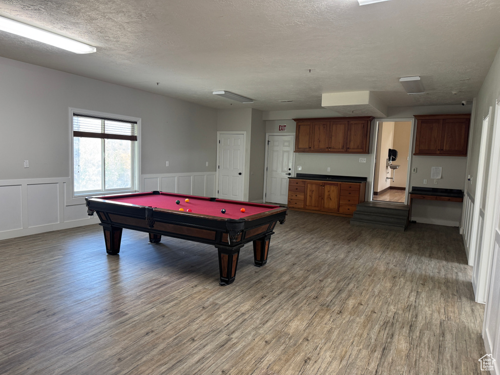 Recreation room featuring light wood-style floors, billiards table, a wainscoted wall, a textured ceiling, and a decorative wall