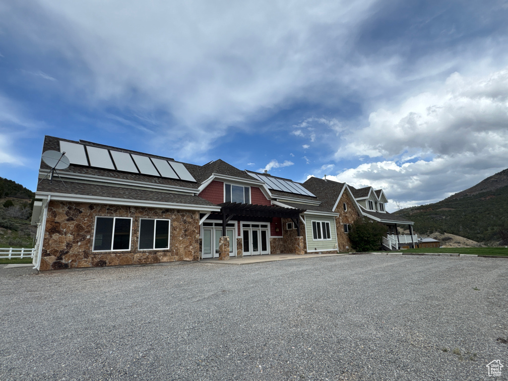 View of front of house featuring french doors, solar panels, a pergola, and stone siding