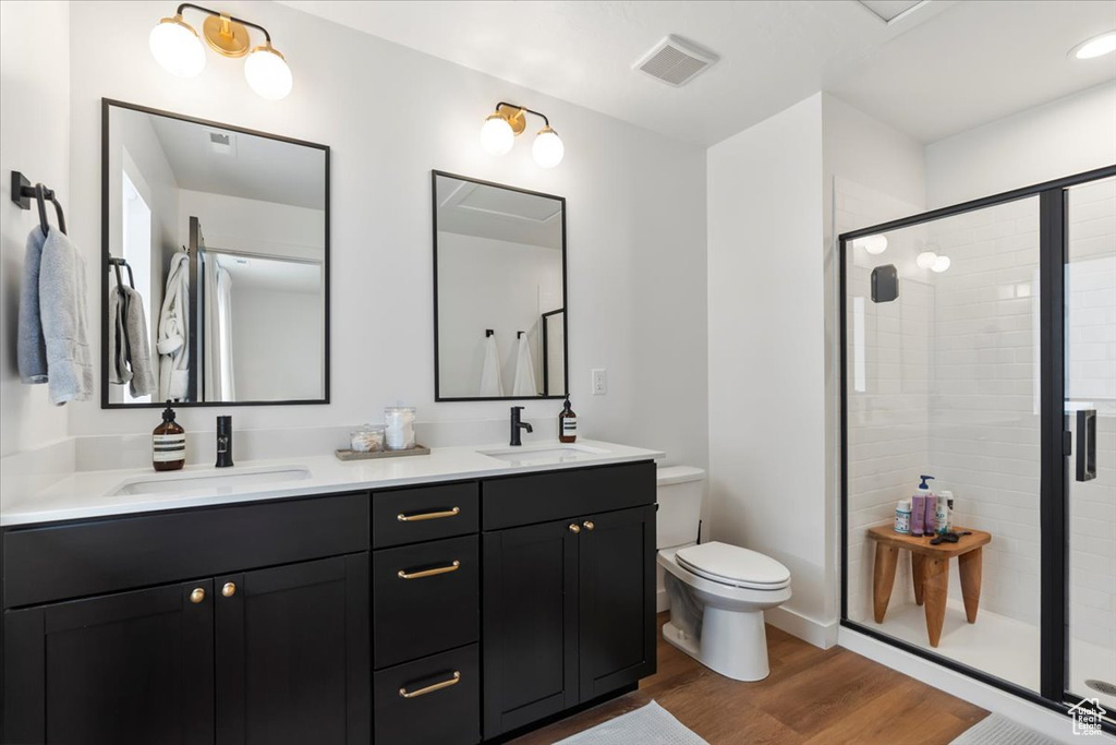 Full bath with a sink, a stall shower, toilet, and wood finished floors