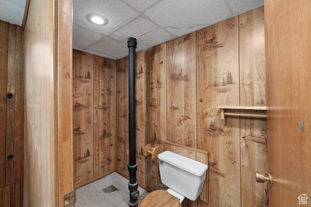 Bathroom with wood walls, a drop ceiling, tile patterned floors, and toilet
