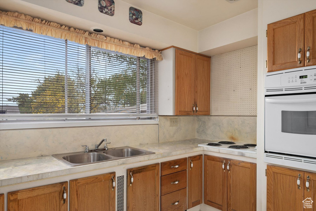 Kitchen with brown cabinets, a sink, white appliances, light countertops, and decorative backsplash