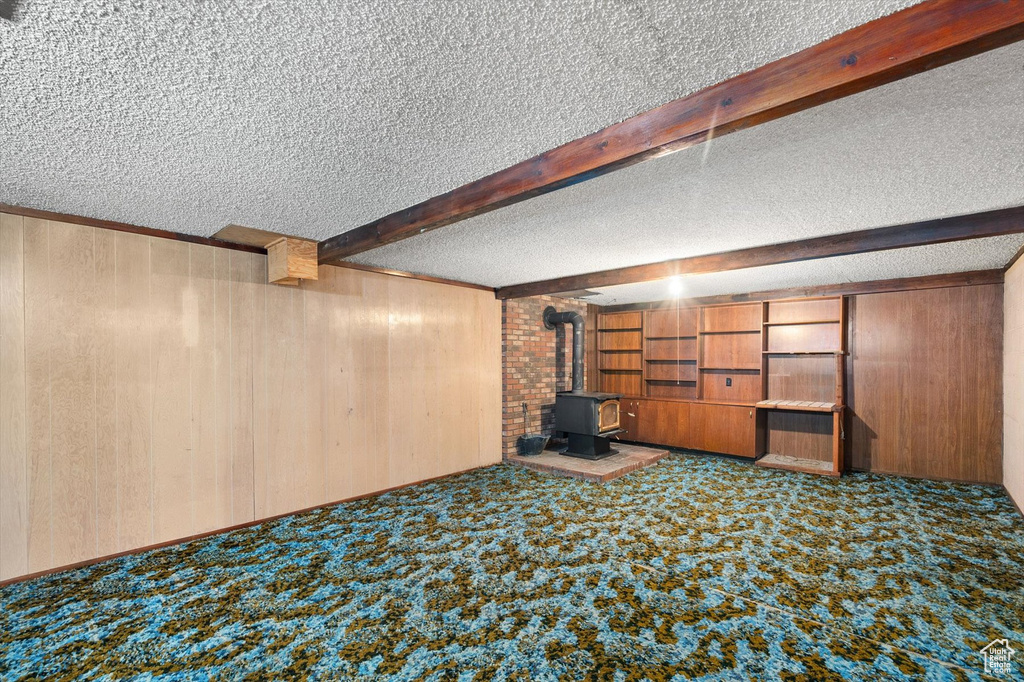 Finished below grade area featuring carpet, a wood stove, wood walls, and a textured ceiling