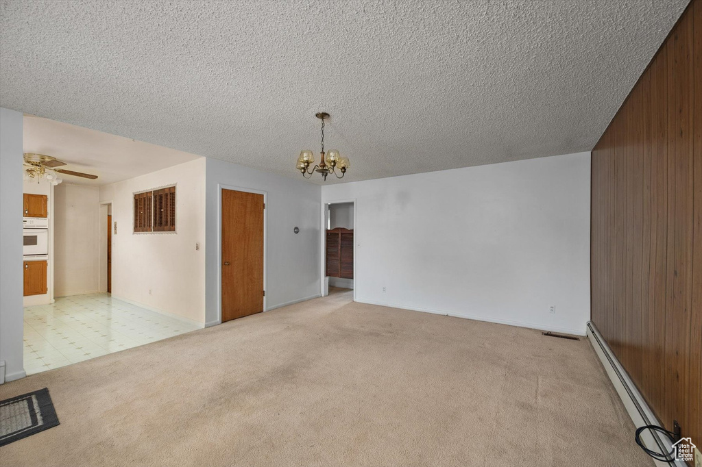Unfurnished room featuring a baseboard heating unit, wood walls, a textured ceiling, and light colored carpet