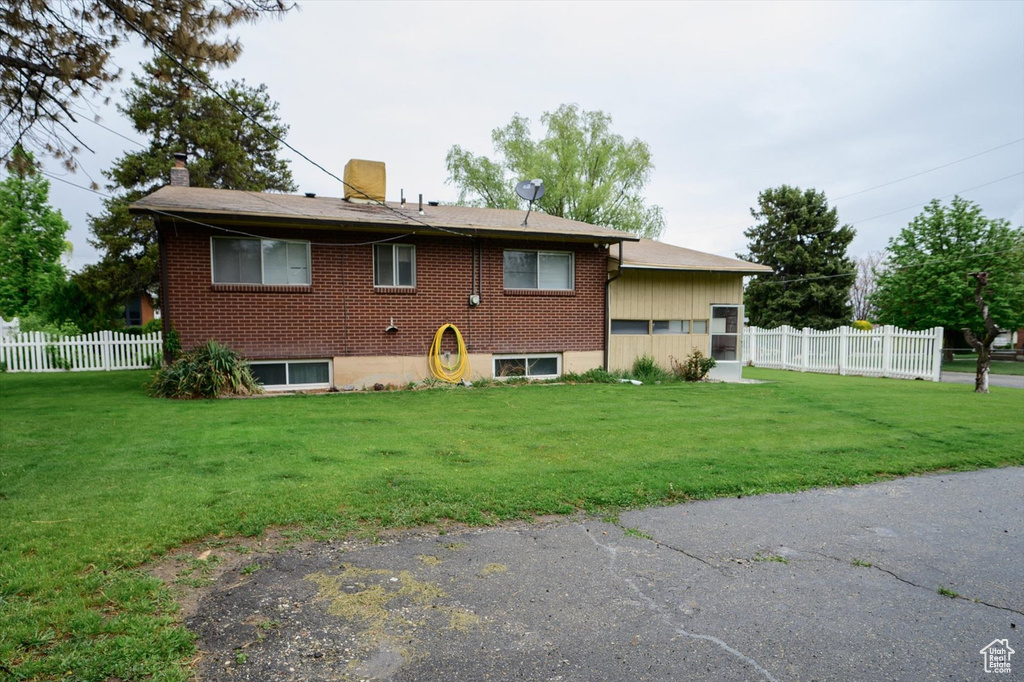 Back of house with a lawn, brick siding, fence, and a chimney