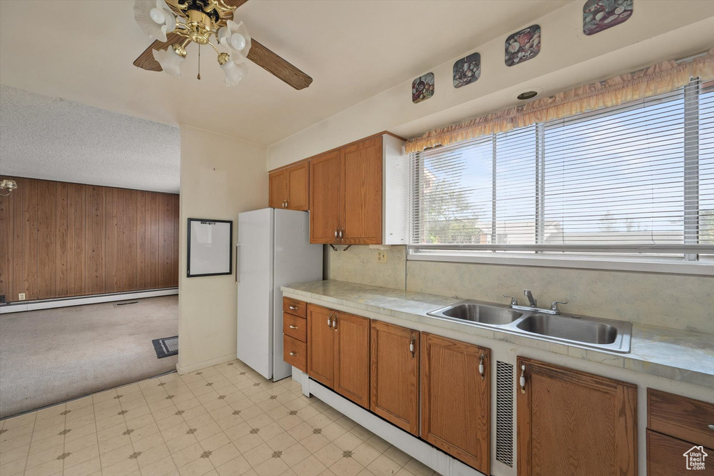 Kitchen featuring brown cabinetry, a ceiling fan, a sink, freestanding refrigerator, and light floors