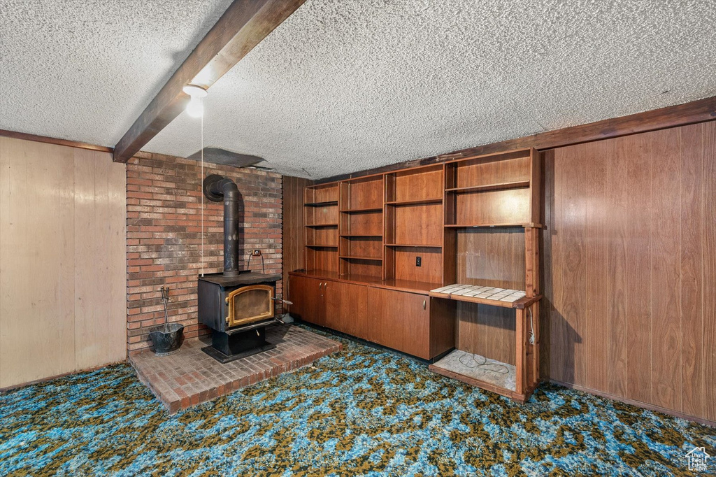 Unfurnished living room with carpet floors, wood walls, a textured ceiling, and a wood stove