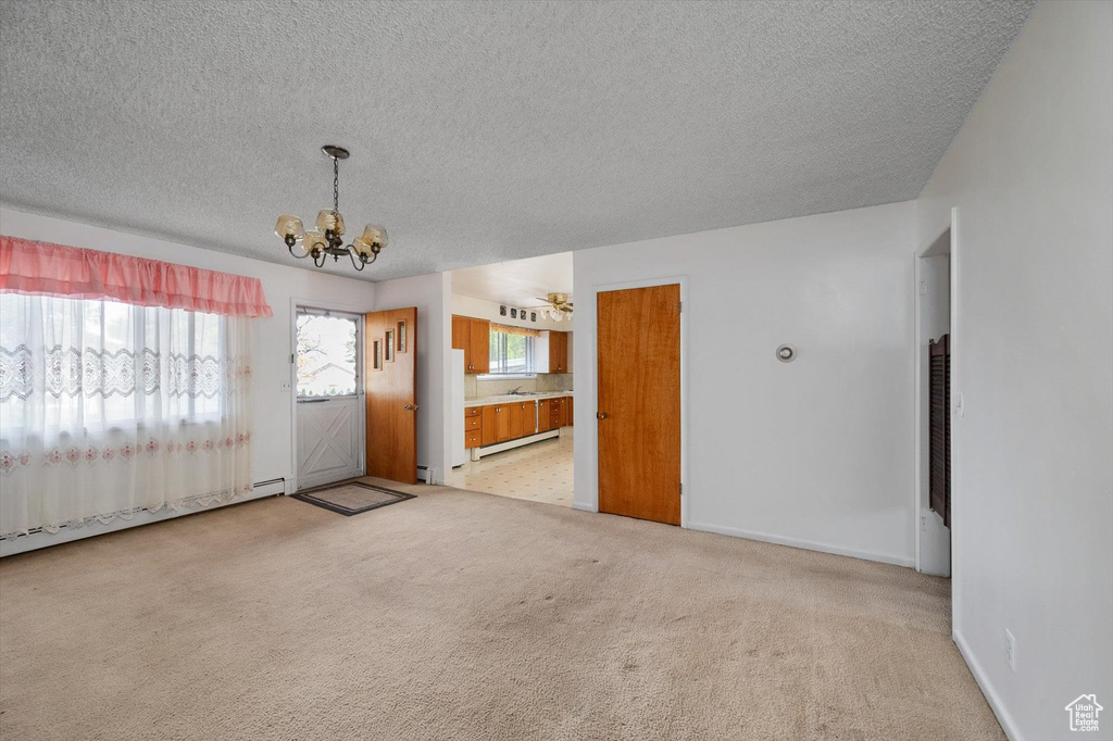 Interior space with a baseboard heating unit, a textured ceiling, a chandelier, and light carpet