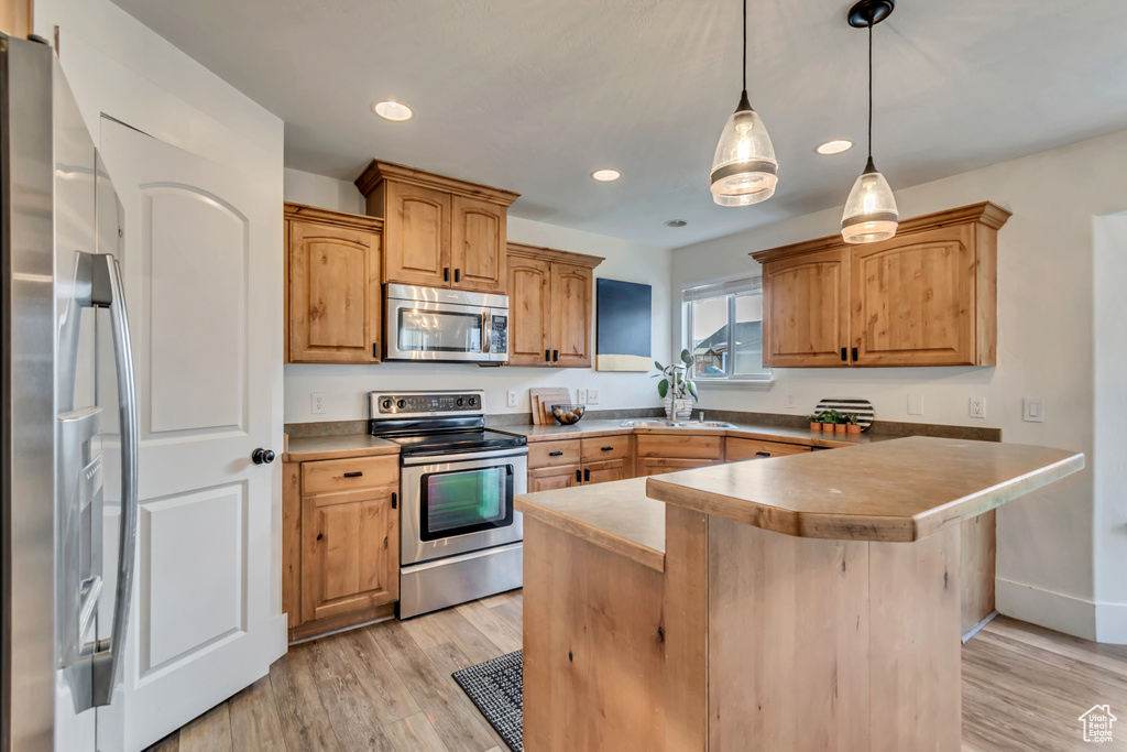 Kitchen with stainless steel appliances, recessed lighting, light wood-style flooring, and decorative light fixtures