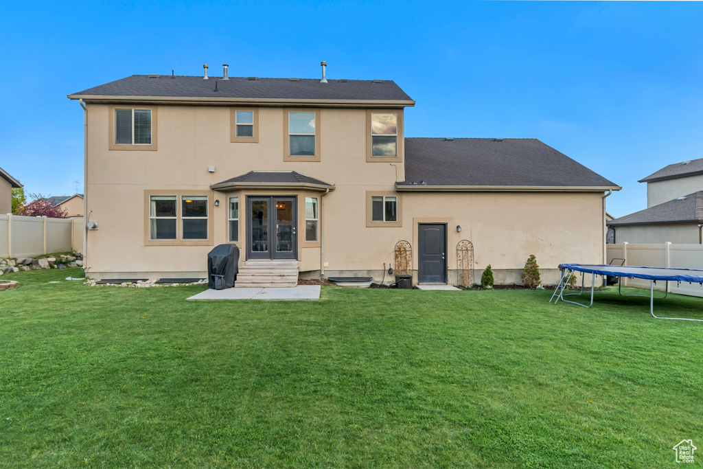 Rear view of property with a lawn, a fenced backyard, a trampoline, and french doors