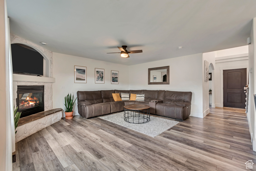 Living room featuring a ceiling fan, baseboards, wood finished floors, and a fireplace