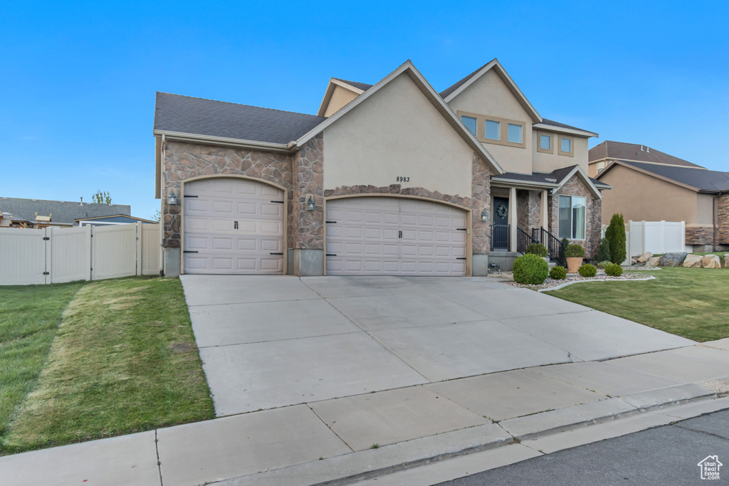 View of front of property with a front yard, stone siding, a gate, concrete driveway, and an attached garage