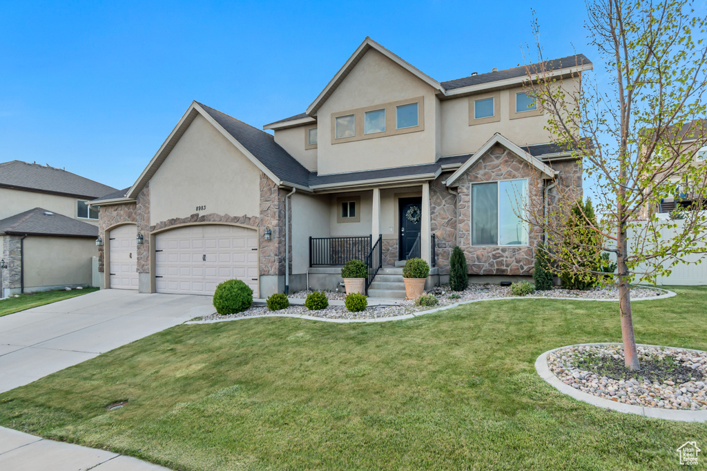 Craftsman house featuring a front yard, concrete driveway, an attached garage, stone siding, and stucco siding