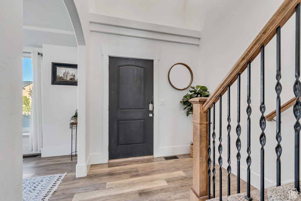 Entryway featuring light wood-style floors, arched walkways, baseboards, visible vents, and stairway