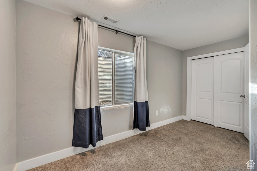 Unfurnished bedroom with visible vents, carpet, baseboards, and a closet