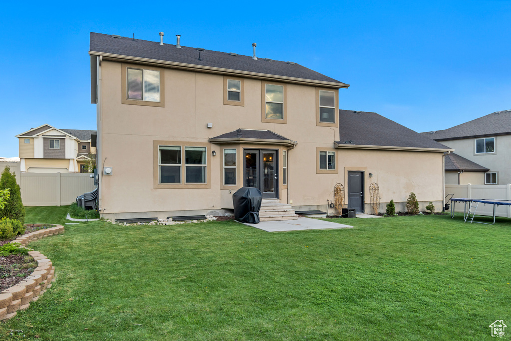 Back of house featuring a lawn, fence, a trampoline, and stucco siding