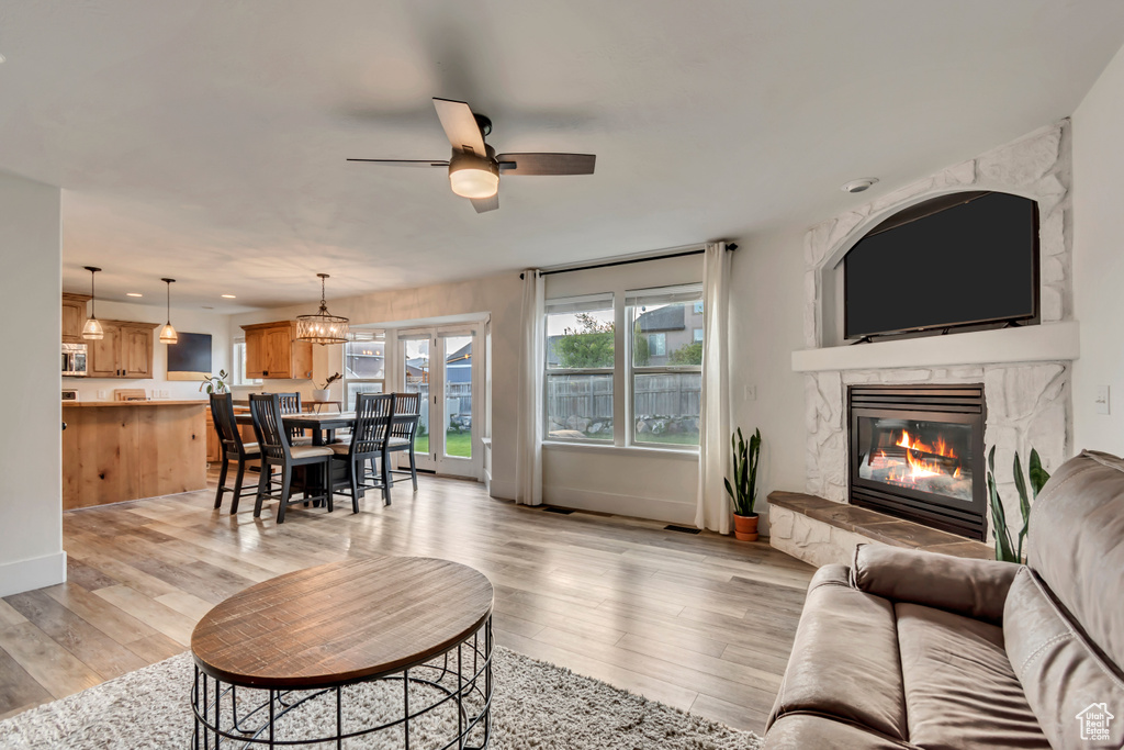 Living area featuring baseboards, ceiling fan, a fireplace, and light wood-style flooring