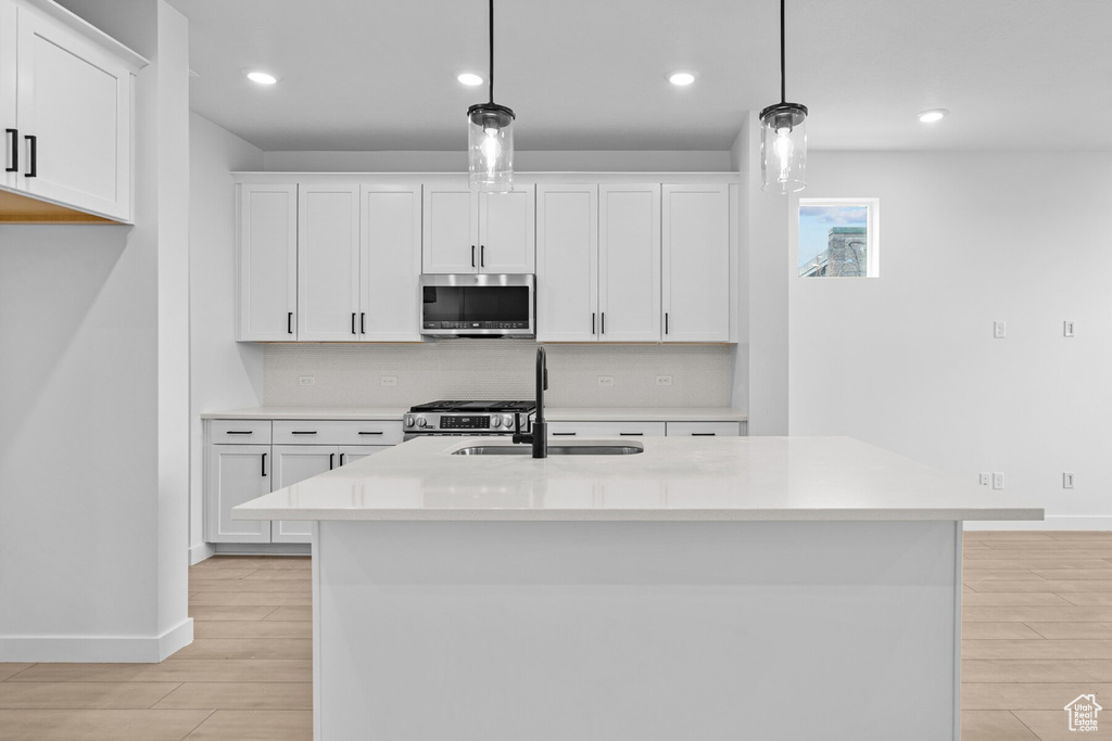 Kitchen with white cabinets, appliances with stainless steel finishes, a sink, light countertops, and light wood-style flooring