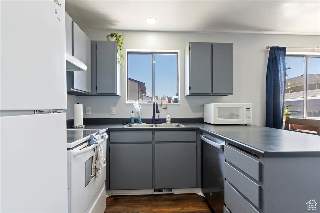 Kitchen with gray cabinetry, a sink, dark countertops, and white appliances