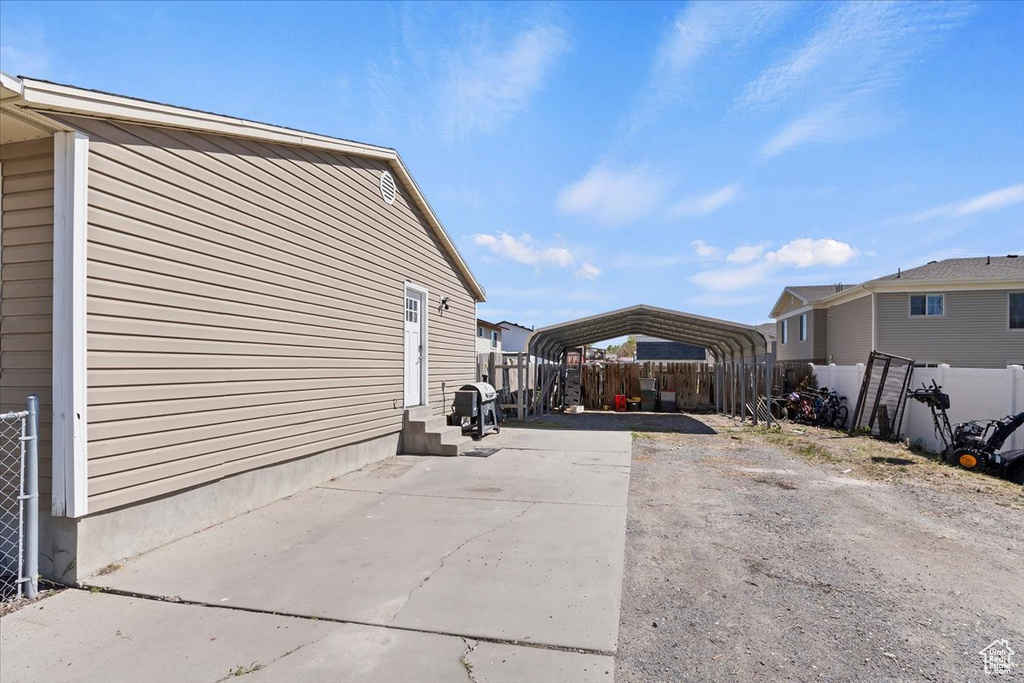 View of property exterior featuring concrete driveway, entry steps, fence, and a detached carport