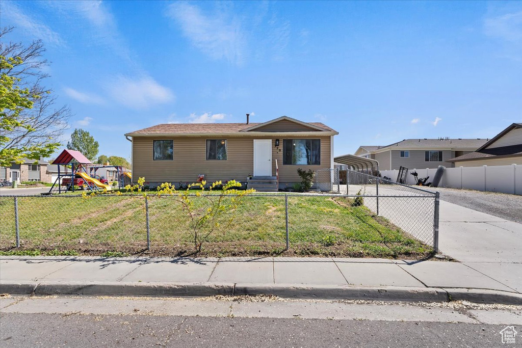 View of front of property featuring a detached carport, a fenced front yard, concrete driveway, and a front lawn