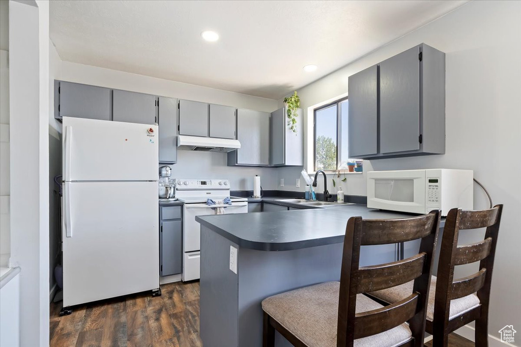 Kitchen with a sink, gray cabinetry, a peninsula, under cabinet range hood, and white appliances