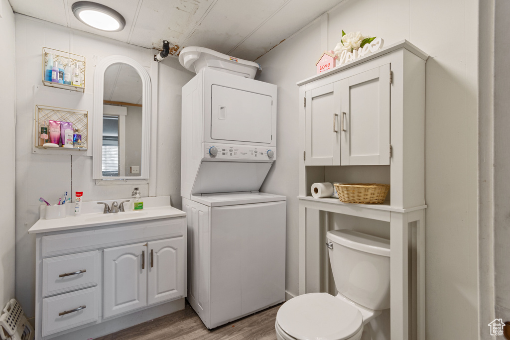 Bathroom featuring wood finished floors, stacked washer / drying machine, toilet, and vanity