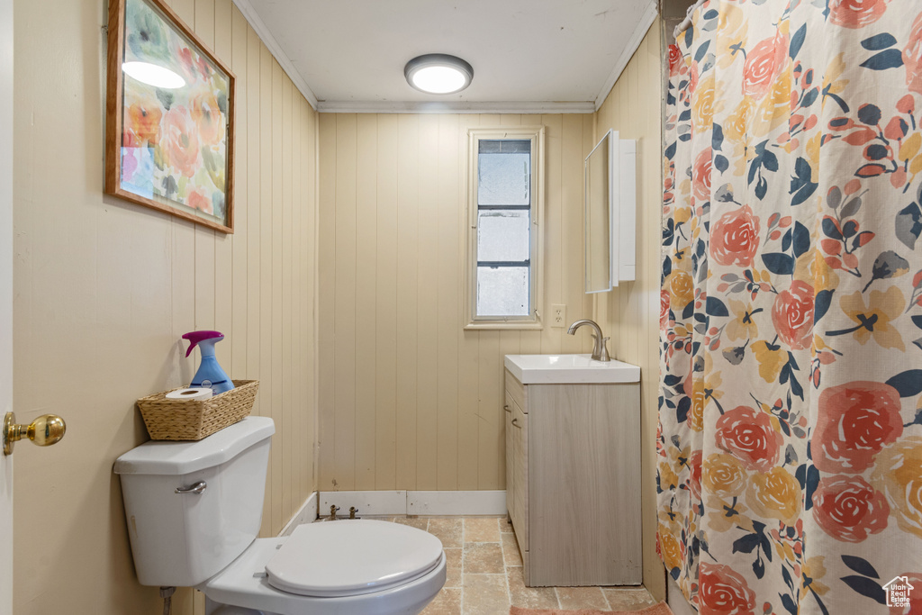 Bathroom with vanity, wood walls, toilet, baseboards, and stone finish flooring