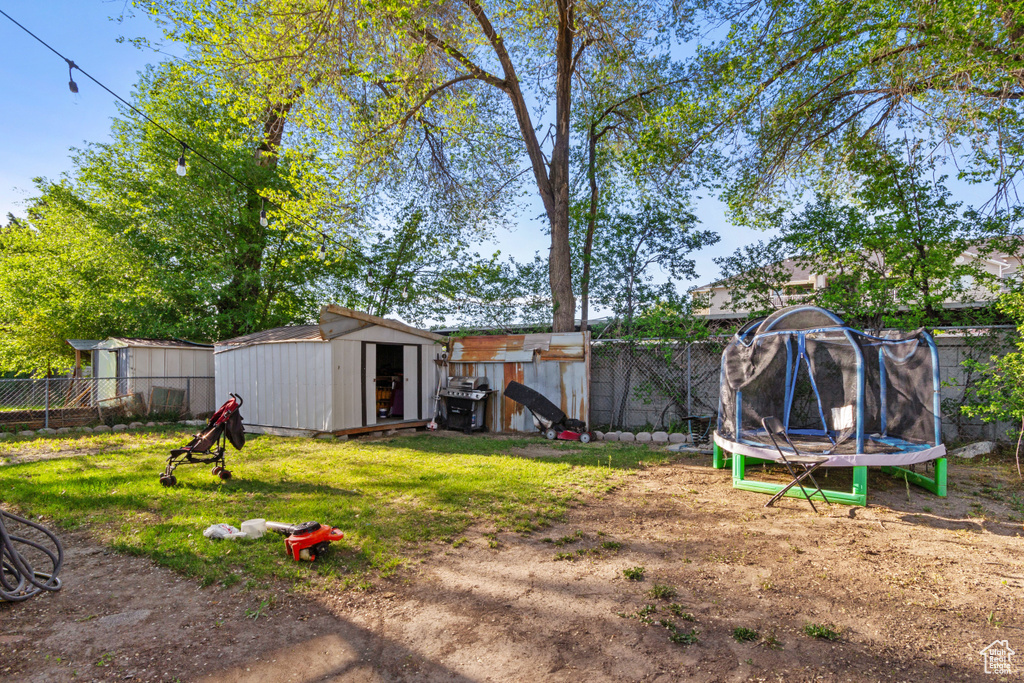 View of yard with a storage unit, a fenced backyard, a trampoline, and an outdoor structure