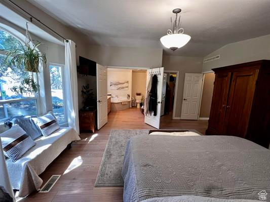 Bedroom with connected bathroom, lofted ceiling, and wood finished floors