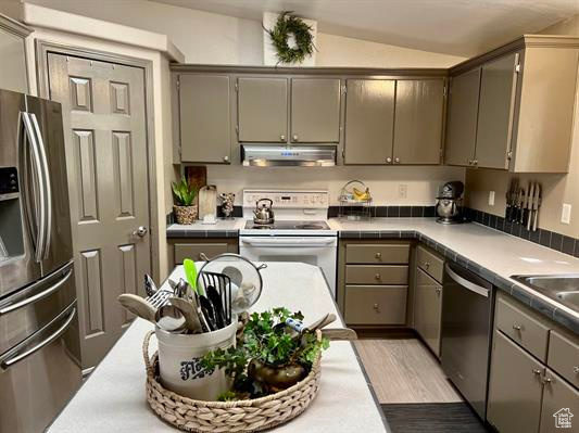 Kitchen featuring under cabinet range hood, stainless steel appliances, tile countertops, and gray cabinets