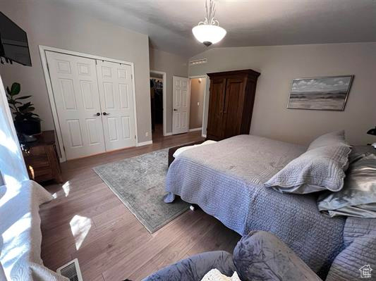 Bedroom with vaulted ceiling, wood finished floors, and a closet