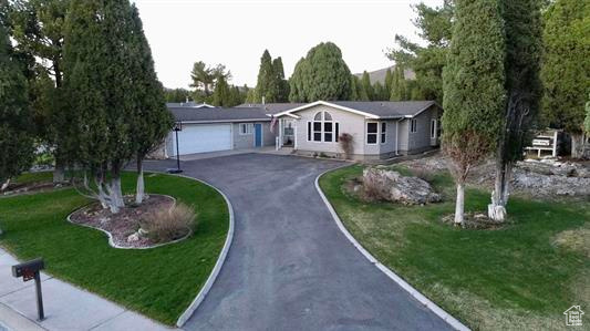 Ranch-style home featuring an attached garage, a front lawn, and aphalt driveway