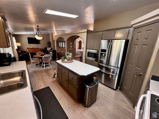 Kitchen with a center island, arched walkways, a sink, light wood-style flooring, and appliances with stainless steel finishes