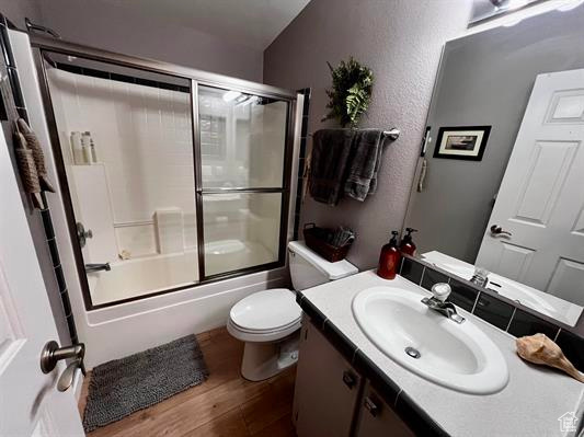 Full bath featuring toilet, wood finished floors, shower / bath combination with glass door, and vanity