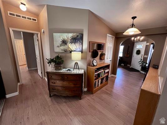 Entrance foyer with arched walkways, baseboards, wood finished floors, vaulted ceiling, and visible vents