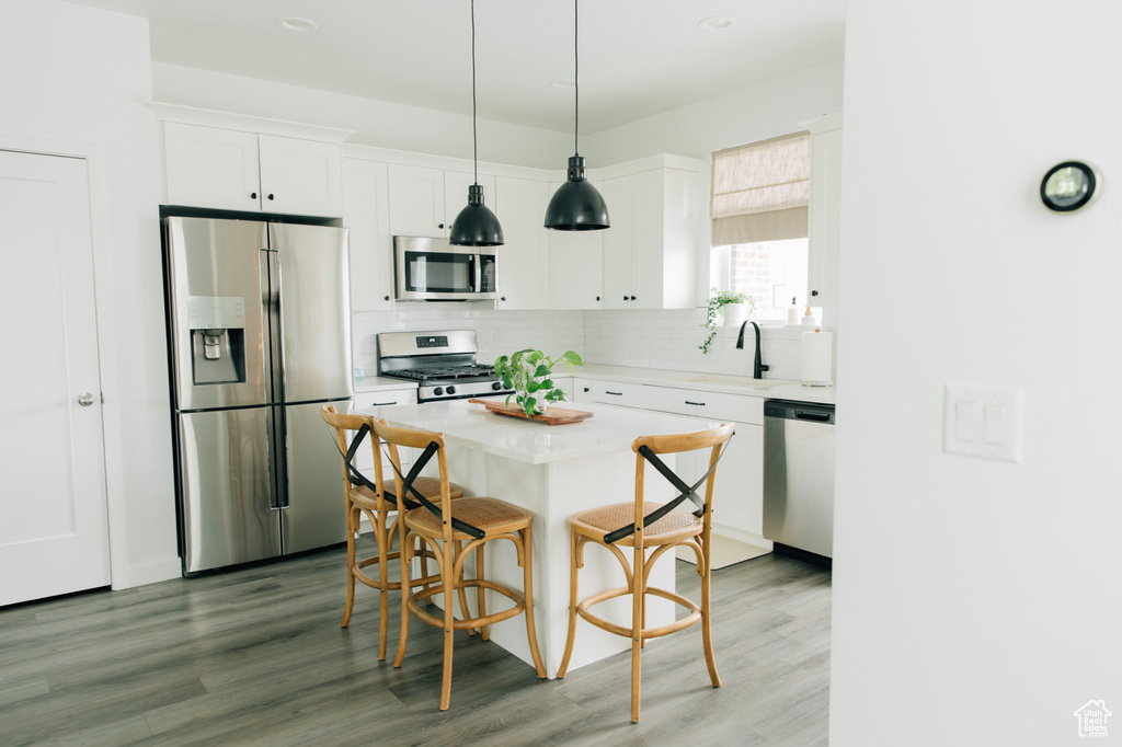 Kitchen with backsplash, appliances with stainless steel finishes, light wood-type flooring, white cabinets, and a breakfast bar