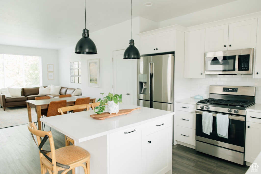 Kitchen with appliances with stainless steel finishes, light countertops, a breakfast bar area, white cabinetry, and dark wood-style floors