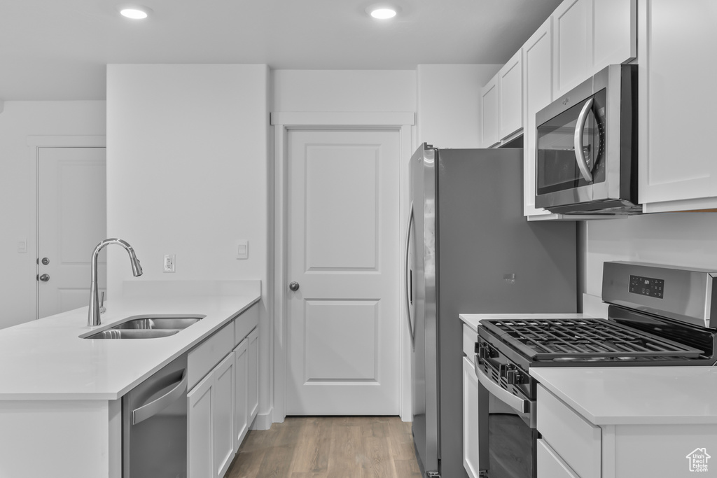 Kitchen with a peninsula, white cabinets, a sink, light wood-style flooring, and stainless steel appliances